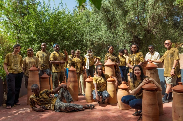 Photo des 15 artistes prise par l'artiste photographe Julie Mvie (Gabon). Ils sont habillés en tissu traditionnel Bogolan (Mali) un emblème historique du patrimoine culturel africain. Son nom, Bogolanfini, signifie en bambara « tissu fait avec la terre », en référence à sa teinture artisanale réalisée à partir de boue fermentée et de pigments naturels. Chaque motif raconte une histoire et porte une signification : courage, sagesse, protection, transmission ou lien avec la nature.