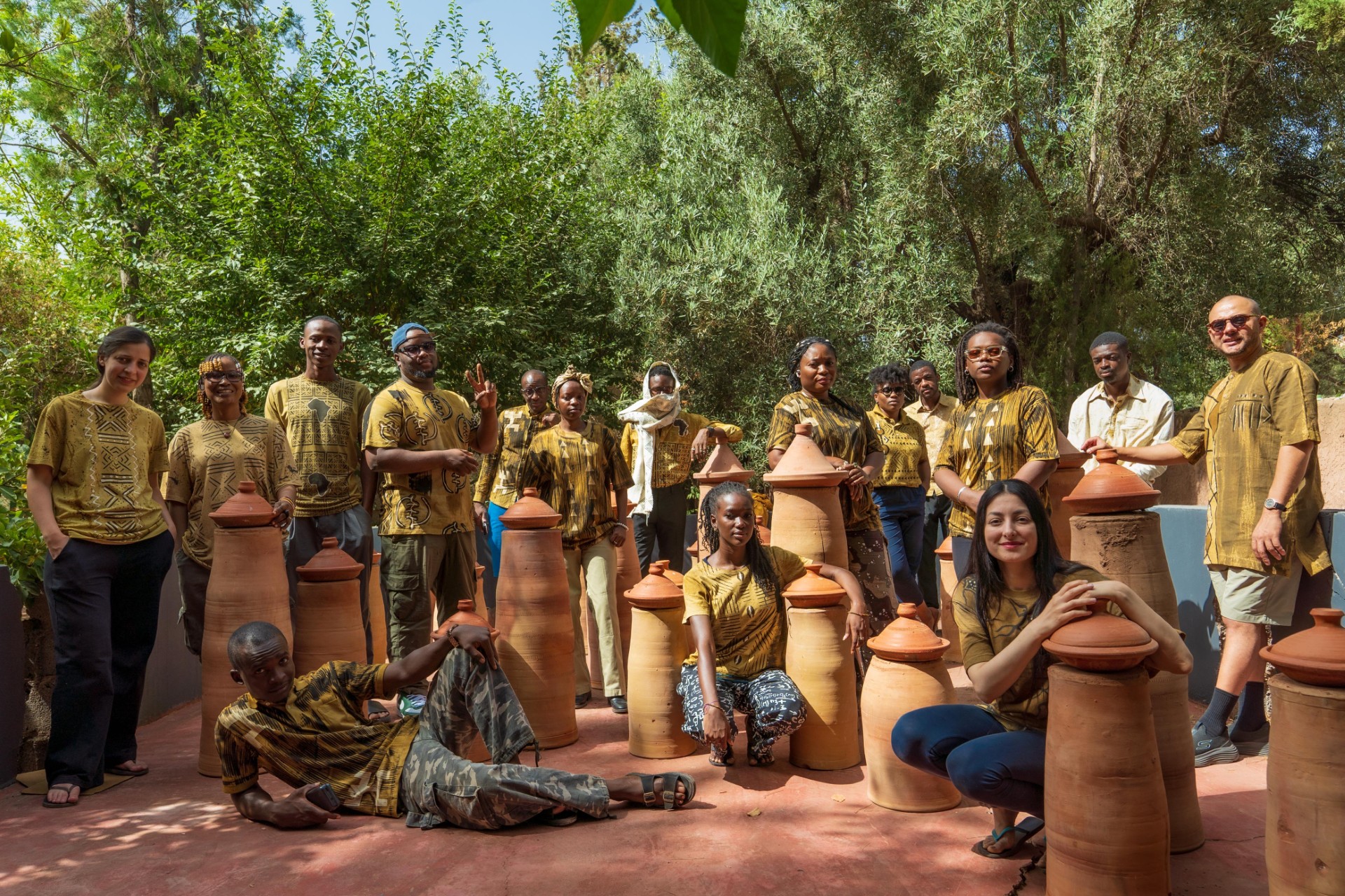 Photo des 15 artistes prise par l'artiste photographe Julie Mvie (Gabon). Ils sont habillés en tissu traditionnel Bogolan (Mali) un emblème historique du patrimoine culturel africain. Son nom, Bogolanfini, signifie en bambara « tissu fait avec la terre », en référence à sa teinture artisanale réalisée à partir de boue fermentée et de pigments naturels. Chaque motif raconte une histoire et porte une signification : courage, sagesse, protection, transmission ou lien avec la nature.